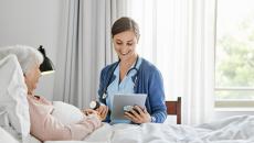 caregiver at patient bedside reviews prescription information with a virtual care prescriber on a tablet   