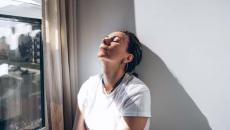 Woman stands by window head against a wall